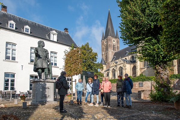 Groep bezoekers krijgt een rondleiding door Thorn met op de achtergrond de Abdijkerk